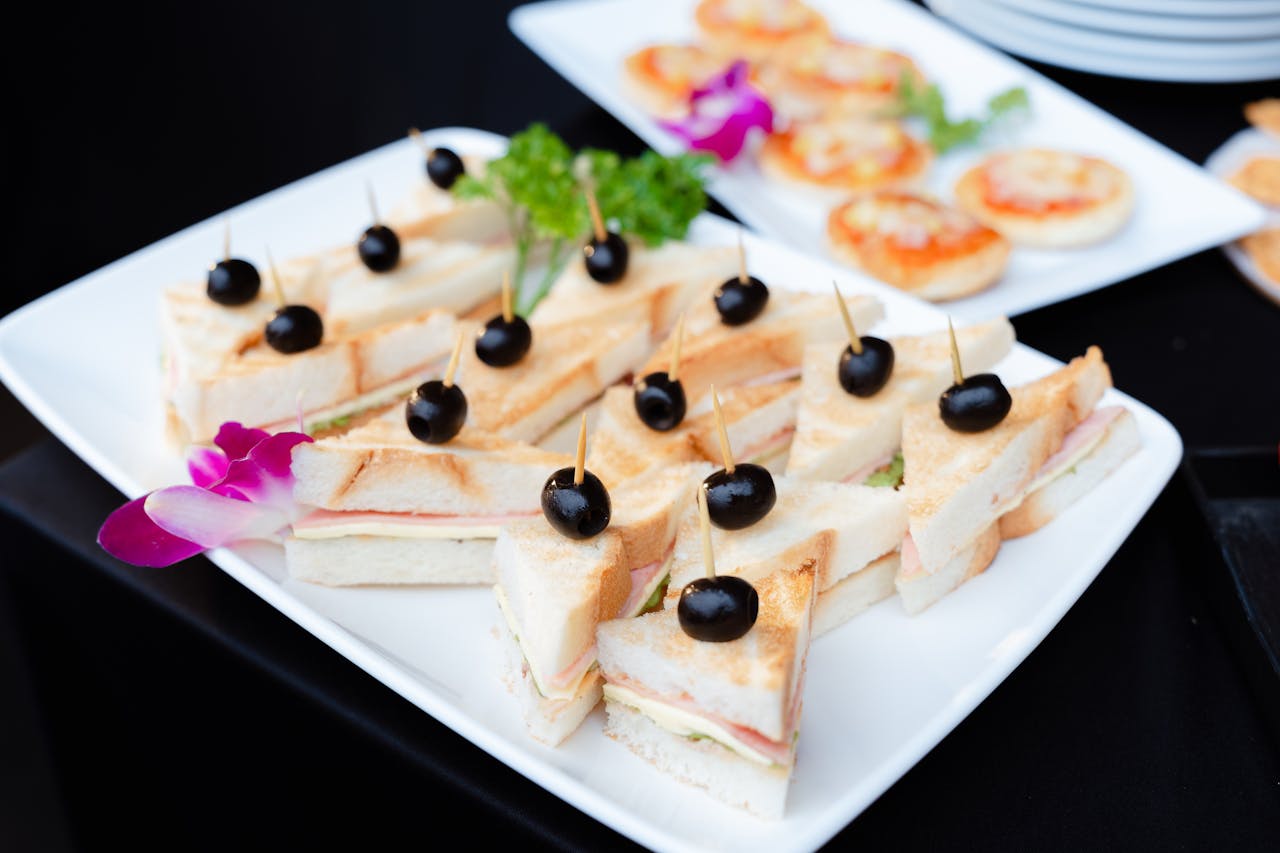 A sophisticated platter of mini sandwiches garnished with black olives, ideal for events.