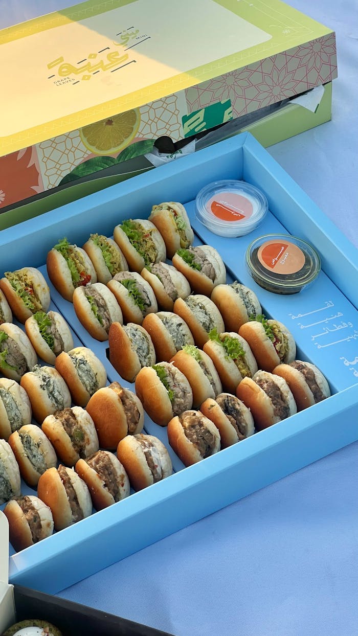 A vibrant box of assorted mini sandwiches with dipping sauces, perfect for parties.
